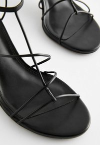 Svarta platta sandaler med en minimalistisk design, tunna korsade remmar och en slät, matt läderfinish. Öppen tå-stil.