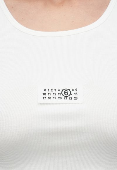 Λευκό τοπ από ριμπ ύφασμα με ετικέτα μεγέθους που εμφανίζει αριθμούς από 0 έως 23, με τον αριθμό 6 να είναι κυκλωμένος με μαύρο.