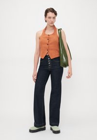 Oransje linne halterneck topp med knappdetalj, parret med mørkeblå høyt liv flared jeans. Akkompagnert med en grønn glossy tote bag.