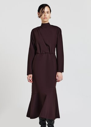 Robe longue marron avec un col haut, une taille cintrée, des manches longues et un ourlet évasé. Faisant en tissu lisse et texturé avec des coutures angulaires.