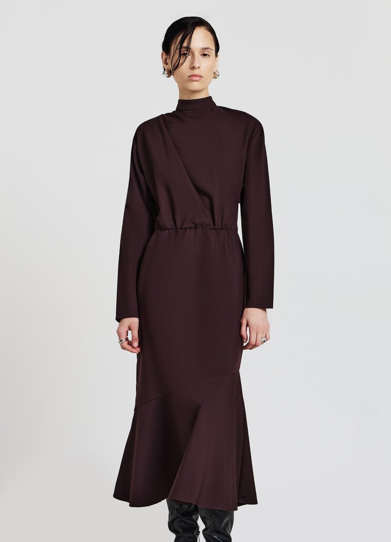 Langes braunes Kleid mit hohem Kragen, tailliertem Schnitt, langen Ärmeln und ausgestellt geschnittenem Saum. Hergestellt aus einem glatten, strukturierten Stoff mit kantigen Nähten.