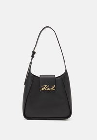 Sac en cuir noir à bandoulière avec une forme structurée, quincaillerie dorée et un rabat avant comportant un détail de signature en cursive.