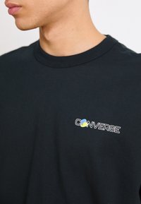 Svart bomull T-skjorte med rund hals og en fargerik "Converse"-logo brodert på venstre bryst. Enkelt, klassisk design.