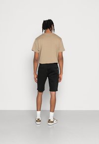 Béžové bavlněné tričko, černé šortky, bílé ponožky do půli lýtek a boty s hnědým akcentem. Krátké rukávy, volný střih a jednoduchý design.