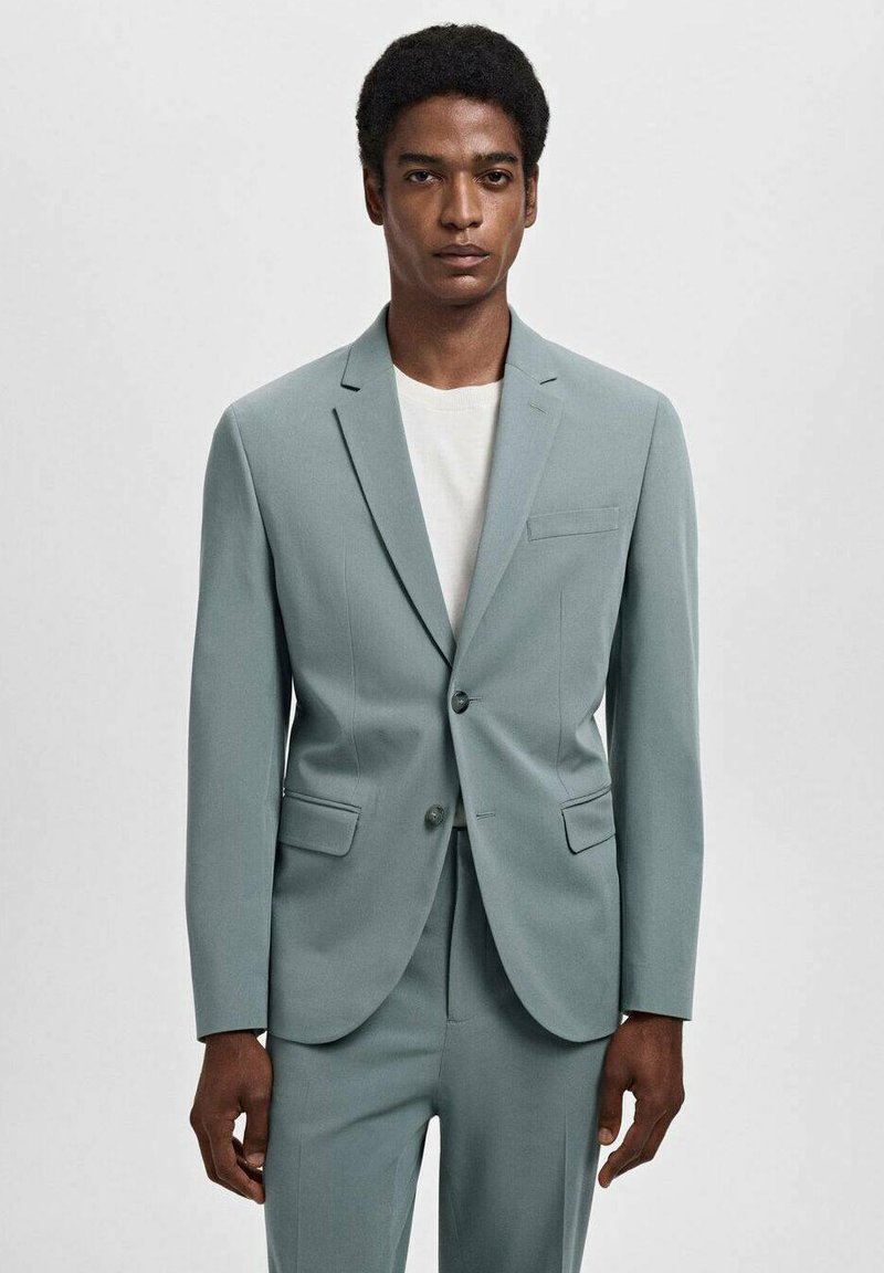 Completo turchese chiaro con giacca strutturata e pantaloni coordinati. La giacca presenta una chiusura a un bottone, rever a punta e tasche frontali.