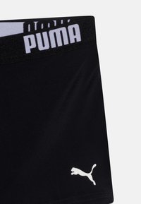 Čierne športové šortky so širokým elastickým pásom, na ktorom je biele písmo "PUMA". Šortky majú malé biele logo na ľavom stehne.