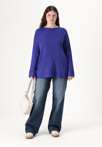 Blauer Strickpullover mit strukturiertem Muster, lockerer Passform und langen Ärmeln, kombiniert mit ausgebleichten blauen weit geschnittenen Jeans und einer hellen Tasche.