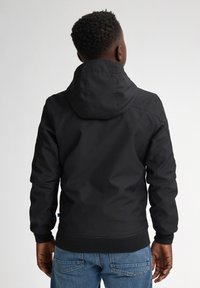 Schwarze Kapuzenjacke mit glatter Textur, elastischen Bündchen und taillierter Saum, über blauen Jeans getragen, von hinten betrachtet.