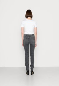 Camiseta blanca de manga corta combinada con jeans ajustados grises. Los jeans tienen dos bolsillos traseros y se llevan con botas de tacón negras.