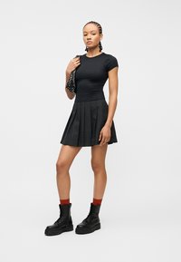 Jauna moteris su pintomis kasomis, dėvinti juodą aptemptą marškinėlį, plisuotą mini sijoną, raudonas kojines, juodus kareiviškus batus ir laikanti juodą maišelį su kniedėmis.