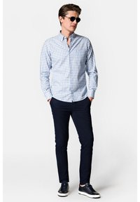 Jasnoniebieska i biała koszula w kratę z długim rękawem, granatowe spodnie slim fit oraz ciemne sneakersy z teksturowanym detalem. Noszone okulary przeciwsłoneczne.