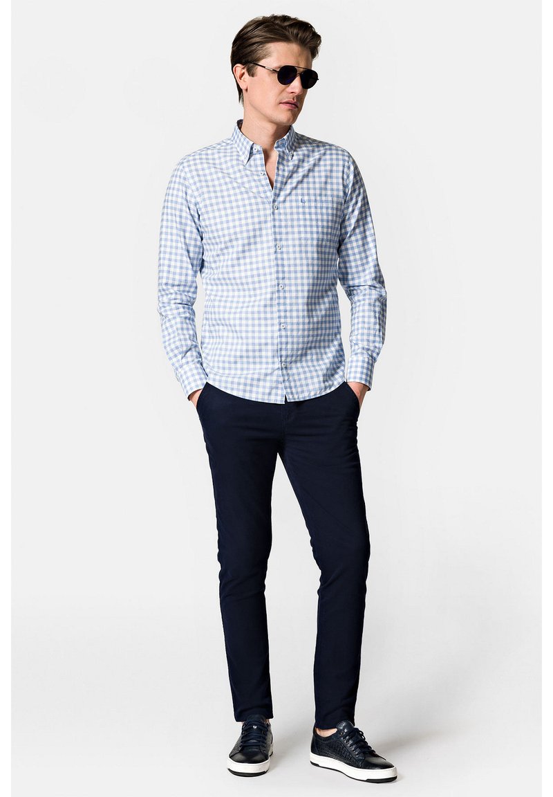 Jasnoniebieska i biała koszula w kratę z długim rękawem, granatowe spodnie slim fit oraz ciemne sneakersy z teksturowanym detalem. Noszone okulary przeciwsłoneczne.