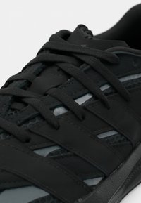 Mustad spordijalats, millel on tekstureeritud pealmine osa, lamedad paelad ja paindlik kummist tald, millel on ventileeritud külgpaneelid ja reljeefsed detailid.