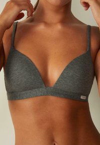 Brassiere en triángulo de algodón gris con tirantes finos, diseño de escote en V profundo y una pequeña etiqueta con logo en la banda inferior. Textura suave y lisa.