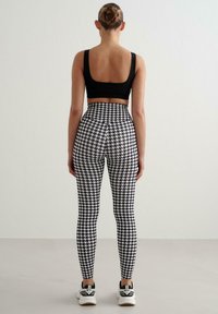 Czarny crop top w połączeniu z legginsami z wysokim stanem ozdobionymi białym wzorem w pepitkę. Minimalistyczny design o gładkiej fakturze i dopasowanym kroju.