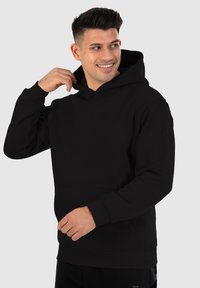 Sudadera negra con capucha en un corte relajado, que presenta un bolsillo frontal y puños de canalé. Textura suave con un branding mínimo en el pecho.