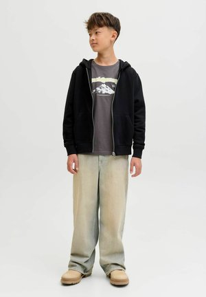 Zwarte zip-up hoodie over een grijs graphic t-shirt, licht vervaagde jeans en beige slip-on schoenen. Bevat twee voorzakken en een ribgebreide mouwe.