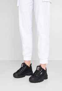 Sorte FILA-sneakers har en kraftig såle, teksturert skinnoverdel, snøring og et merkelogo-detall på tungen.