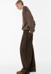 Brun stickad tröja med ribbade detaljer, tillsammans med vida mönstrade byxor i mörkbrunt och grönt. Suedebruna skor fulländar looken.