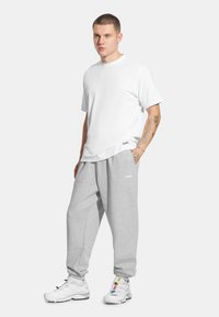 Biała koszulka z krótkim rękawem w połączeniu z jasnoszarymi dresami. Dresy mają elastyczny pas i detal z logo; buty są białe z wielokolorowymi akcentami.