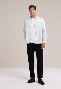 Lichtblauwe overhemden met knopen over een wit T-shirt, gecombineerd met donkere broeken en zwarte schoenen; soepele stof en eenvoudige snit.