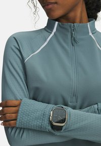 Light blue athletic top with a zippered mock neck, white accent stitching, and textured cuffs. A smartwatch is worn on the left wrist.