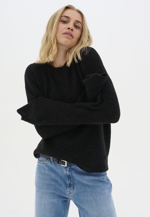 Black knit sweater with a relaxed fit and wide sleeves, paired with light blue jeans and a black belt featuring a silver buckle.