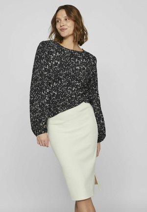 Blusa negra con un patrón salpicado de blanco, de mangas largas, combinada con una falda lápiz ajustada de color verde claro que presenta una abertura lateral.