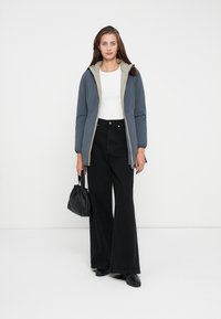 Padded jacket in gray with a light lining, featuring a zip closure and hood. Paired with black flared pants and a black bag.