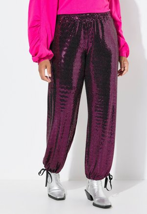 Pantalons de jogger en sequins dégradés de rose et noir, avec une taille élastique, des chevilles resserrées et des détails en lien. Des bottines argentées sont portées.