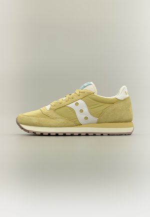 Lysegul og beige ruskind- og stofsneaker med hvidt logo og gummisål, vist fra siden på neutral baggrund.