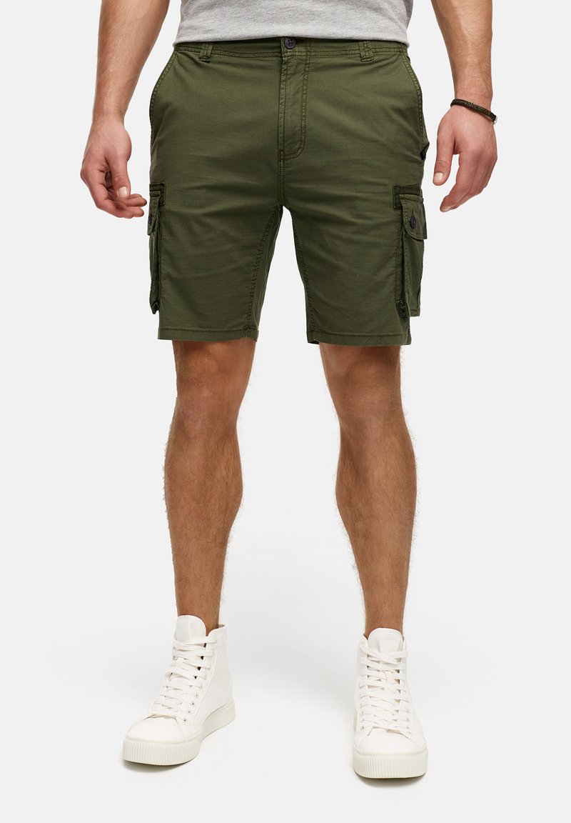 Shorts cargo vert olive avec plusieurs poches latérales, en tissu léger, et coupe droite. Associés à des baskets montantes blanches.