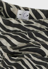Zebramönstrad tyg med svarta och off-white ränder, med sömdetaljer och en knappstängning vid midjan.