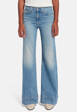 Lichtblauwe denim jeans met brede pijpen, opgerolde boorden en vervaging op de dijen, gedragen met beige puntige schoenen en een wit topje.