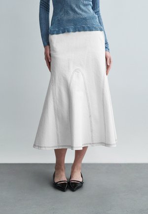 Fehér pamut midi szoknya, bővülő alsó résszel, kontrasztos varrással és sima textúrával. Fekete hegyes orrú cipővel párosítva.
