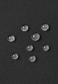 Klarer Wassertropfen auf strukturiertem schwarzem Stoff, unterschiedlich in der Größe, die ihre sphärische Form und reflektierenden Oberflächen zeigen.