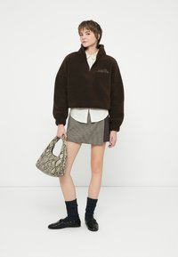 Pulover din fleece maro cu fermoar pe un sfert, cămașă albă cu guler dedesubt, fustă mini în carouri, loafers negri și o geantă cu model de piele de șarpe.