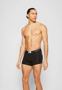 Juodi Calvin Klein bokseriai su minkšta tekstūra ir elastiniu diržu su logotipu, pasižymintys prigludusia išvaizda ir vidurinio šlaunies ilgiu.