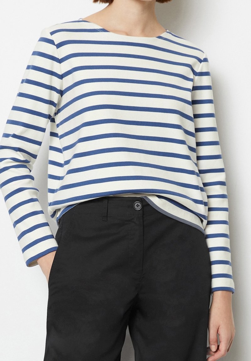Gestreiftes Langarmshirt mit blauen und weißen Streifen, runder Ausschnitt und weichem Stoff, kombiniert mit schwarzen Hosen mit einem Knopfdetail.