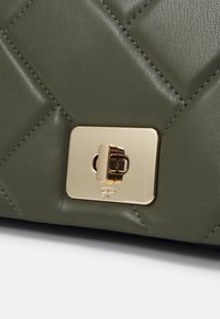 Zelená prošívaná kožená kabelka s obdélníkovým zlat�ým zapínáním a jemnými švy, které zdůrazňují texturovaný povrch.