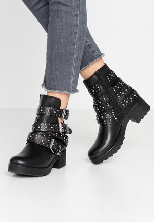 Black ankle boots with multiple studded straps and buckles, featuring a chunky heel and a textured sole. Zipper closure at the back.