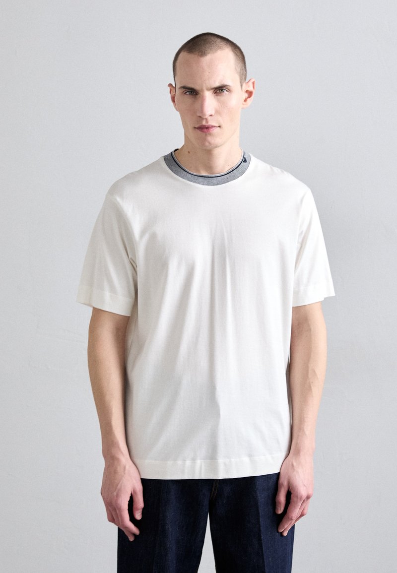 Šviesiai kreminės spalvos trumpomis rankovėmis, apvalios iškirptės marškinėliai su kontrastinga pilka vidine apykakle. Pagaminti iš minkštos medžiagos; laisvas fasonas; minimalistiškas dizainas.