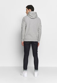 Grijze hoodie met een grote capuchon, geribbelde manchetten en onderkant, gecombineerd met een paar donkere spijkerbroeken en witte sneakers, bekeken vanuit de achterkant.