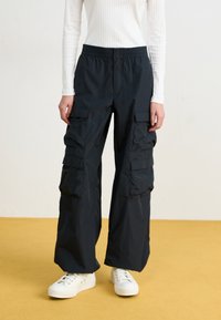 Svarte cargo-bukser med vide ben, elastisk livlinje og flere store lommer. Laget av et glatt, lett stoff.