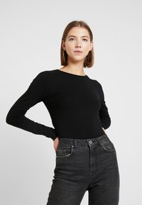 Schwarzes Langarmoberteil mit Rundhalsausschnitt, kombiniert mit hoch taillierten dunkelgrauen Jeans. Glatte Stoffqualität mit einer figurbetonten Silhouette.