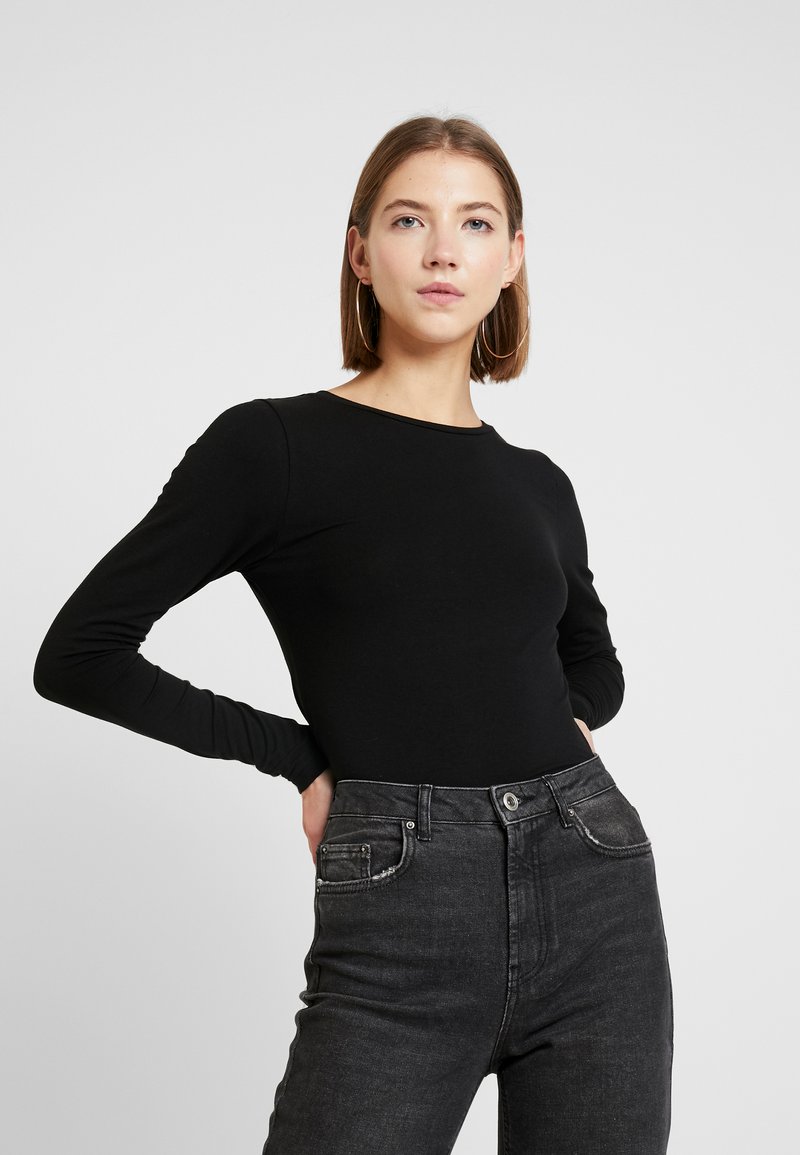 Schwarzes Langarmoberteil mit Rundhalsausschnitt, kombiniert mit hoch taillierten dunkelgrauen Jeans. Glatte Stoffqualität mit einer figurbetonten Silhouette.