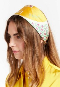 Un foulard présentant un haut en satin jaune avec "Paris" imprimé, et une section inférieure à motifs en vert avec des motifs floraux.
