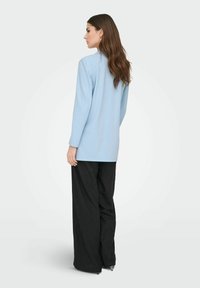 Gaiši zils garām piedurknēm tops ar taisnu griezumu, kombinēts ar augstu jostasvietu melnām platām biksēm. Gluda tekstūra, vienkāršs dizains.