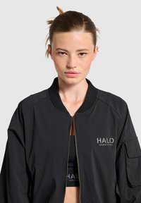 Czarna kurtka bomberka z zamkiem z przodu, żebrowanym kołnierzem i boczną kieszenią. Posiada srebrne logo "HALO" oraz teksturowany materiał.