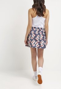 Woman walking away wearing a white tank top, floral navy blue skirt, white socks, and white sneakers with gum soles against a plain background.